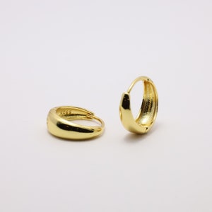 May include: A pair of gold hoop earrings. The earrings are smooth and have a slightly rounded shape.