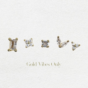 Può includere: Cinque orecchini d'oro con pietre di zircone cubico trasparenti. Gli orecchini hanno la forma di un rettangolo, una stella a quattro punte, un quadrato, una foglia e un triangolo.