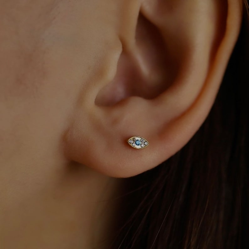 May include: A gold evil eye earring with a blue center stone and white diamond accents.