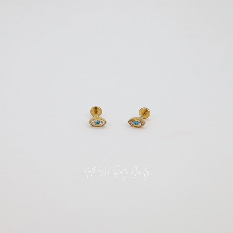 May include: A pair of gold-toned earrings with a blue and white eye design. The earrings are small and delicate, and they would make a great gift for someone who loves unique jewelry.