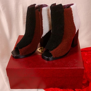 Könnte beinhalten: High-Heel-Stiefeletten mit offenem Zehenbereich und Farbblockdesign in Schwarz, Braun und Weiß. Die Stiefel sind aus einem flauschigen Material gefertigt und haben einen klobigen Absatz. Sie werden auf einer roten Box präsentiert.