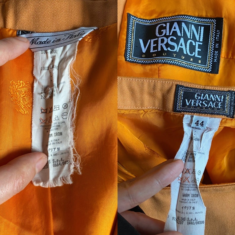 May include: Orange silk pants with a Gianni Versace Couture label and size tag. The label is black with white text and the size tag is white with black text. The pants have a gold embroidered design.