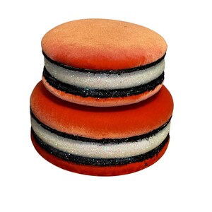May include: Two stacked orange velvet macarons with black and white glitter trim.