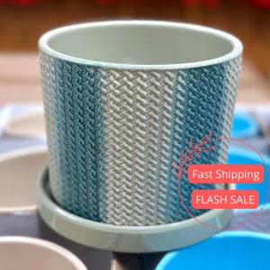 May include: A light blue and white striped ceramic planter with a matching saucer. The planter has a textured surface and a slightly flared rim.