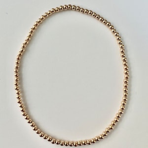 Könnte beinhalten: Ein goldfarbenes Perlenarmband mit schlichtem Design. Das Armband besteht aus kleinen, runden Perlen, die zu einer durchgehenden Schleife zusammengefügt sind.