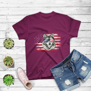 May include: A maroon t-shirt with a graphic of a wolf wearing sunglasses in front of an American flag.