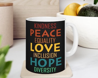 May include: White ceramic mug with a black background and colorful text that reads "Kindness, Peace, Equality, Love, Inclusion, Hope, Diversity".