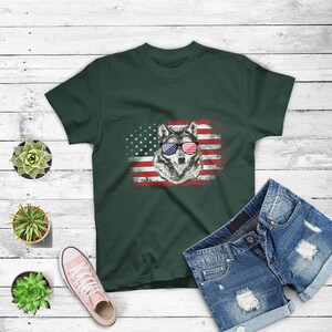 May include: A dark green t-shirt with a graphic of a wolf wearing red, white, and blue sunglasses in front of an American flag.