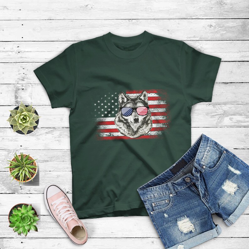 May include: A dark green t-shirt with a graphic of a wolf wearing red, white, and blue sunglasses in front of an American flag.