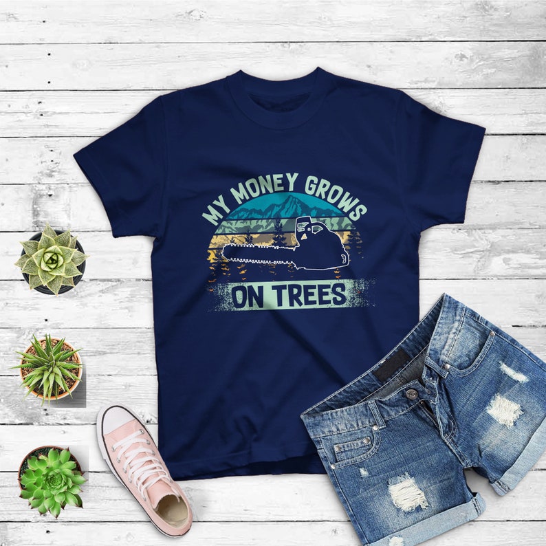 May include: A navy blue t-shirt with a vintage-style graphic of a chainsaw cutting down a tree. The text "My Money Grows On Trees" is printed on the shirt.