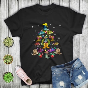 Könnte beinhalten: Schwarzes T-Shirt mit einem Weihnachtsbaum-Design aus Cowboy-Stiefeln und Hüten. Der Baum ist mit Lichtern und Ornamenten geschmückt.