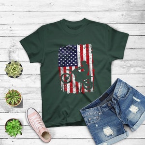 May include: A dark green t-shirt with a distressed American flag design featuring a silhouette of a person riding a dirt bike.