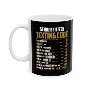 May include: White ceramic coffee mug with a black design. The design features the text "Senior Citizen Texting Code" in gold lettering. The text is followed by a list of common senior citizen texting abbreviations and their meanings.
