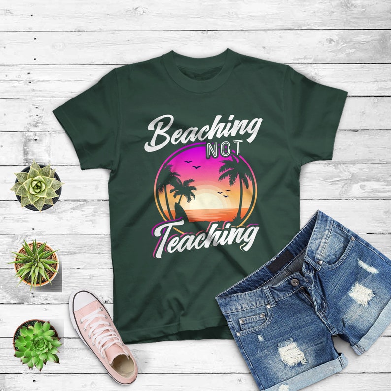 May include: Dark green t-shirt with the text "Beaching Not Teaching" in white and pink. The graphic features a sunset scene with palm trees. Blue denim shorts and pink sneakers are also in the image.