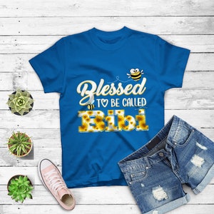 May include: A royal blue t-shirt with a graphic design of a bee and sunflowers. The text on the shirt reads "Blessed to be called Bibi".