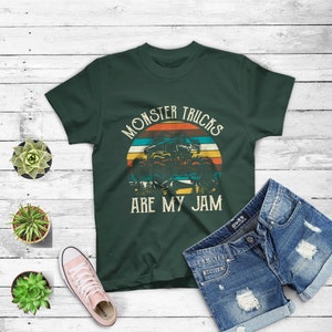 Puede incluir: Una camiseta verde oscuro con un gr&aacute;fico de estilo vintage de un cami&oacute;n monstruo conduciendo a trav&eacute;s de una puesta de sol. El texto "Monster Trucks Are My Jam" est&aacute; impreso en la camiseta.