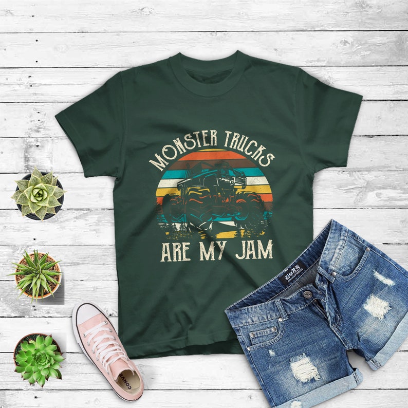 Puede incluir: Una camiseta verde oscuro con un gr&aacute;fico de estilo vintage de un cami&oacute;n monstruo conduciendo a trav&eacute;s de una puesta de sol. El texto "Monster Trucks Are My Jam" est&aacute; impreso en la camiseta.