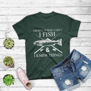 Könnte beinhalten: Ein dunkelgrünes T-Shirt mit einem weißen Grafikdesign, auf dem "That's what I do I fish & I know things" steht. Die Grafik enthält auch einen Fisch und zwei gekreuzte Angelruten.