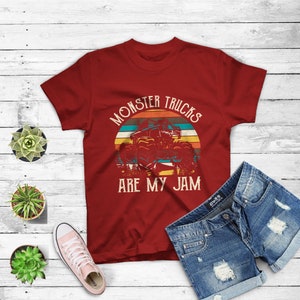 Puede incluir: Camiseta roja con un gr&aacute;fico de estilo vintage de un cami&oacute;n monstruo conduciendo a trav&eacute;s de una puesta de sol. El texto "Monster Trucks Are My Jam" est&aacute; impreso en la camiseta.