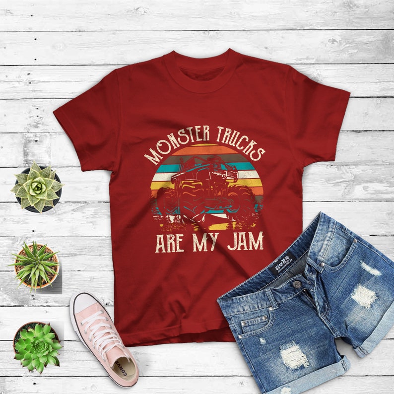 Puede incluir: Camiseta roja con un gr&aacute;fico de estilo vintage de un cami&oacute;n monstruo conduciendo a trav&eacute;s de una puesta de sol. El texto "Monster Trucks Are My Jam" est&aacute; impreso en la camiseta.