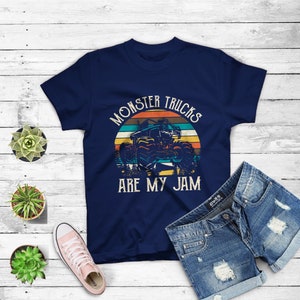 Puede incluir: Una camiseta azul marino con un gr&aacute;fico de estilo vintage de un cami&oacute;n monstruo conduciendo a trav&eacute;s de una puesta de sol. El texto "Monster Trucks Are My Jam" est&aacute; impreso en la camiseta.