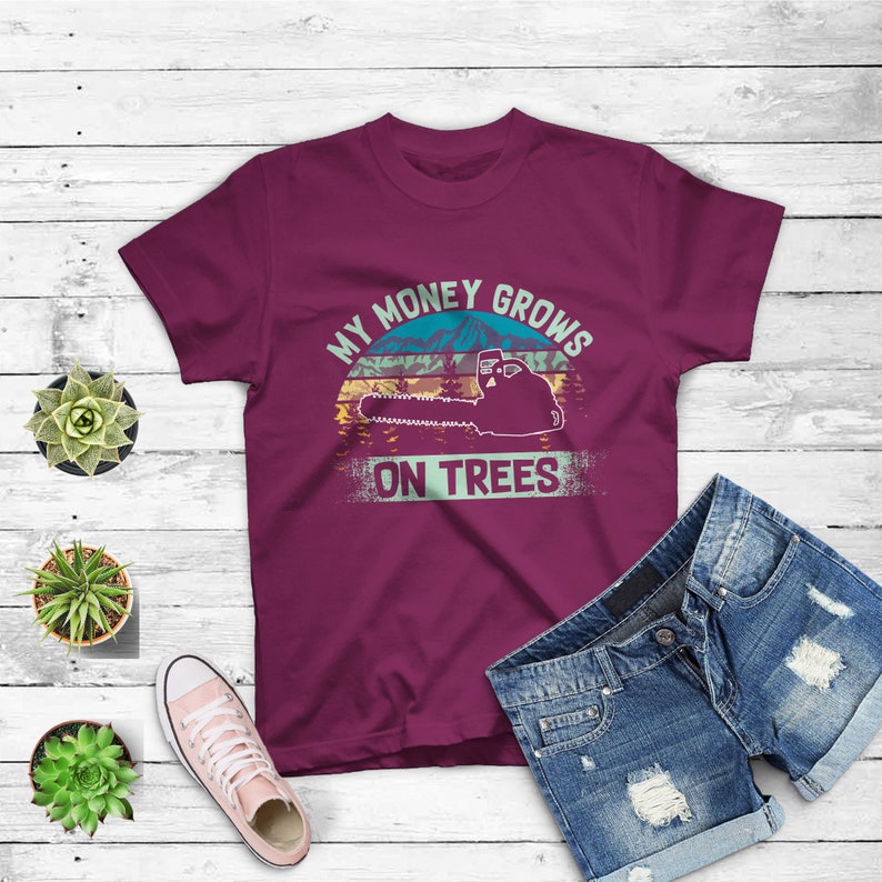 May include: A maroon t-shirt with a vintage-style graphic of a chainsaw cutting down a tree. The graphic says "My Money Grows On Trees".