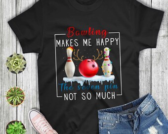 May include: Black t-shirt with a white outline of a bowling ball, two bowling pins with Christmas lights, and a reindeer. The text reads "Bowling makes me happy. The seven pin not so much."