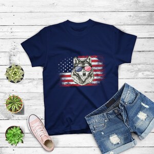 May include: A navy blue t-shirt with a distressed American flag design featuring a wolf wearing red, white, and blue sunglasses.