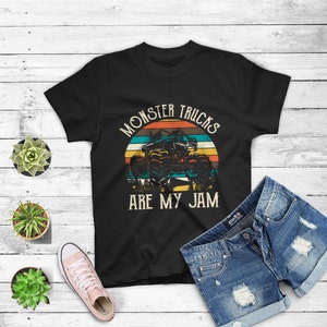 Puede incluir: Camiseta negra con un gr&aacute;fico de estilo vintage de un cami&oacute;n monstruo conduciendo a trav&eacute;s de una puesta de sol. El texto "Monster Trucks Are My Jam" est&aacute; impreso en la camiseta.