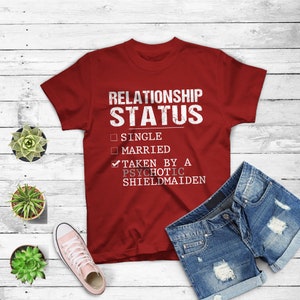 May include: Red t-shirt with a white graphic that says "Relationship Status" with a checkmark next to "Taken by a Psychotic Shieldmaiden" and unchecked boxes next to "Single" and "Married".