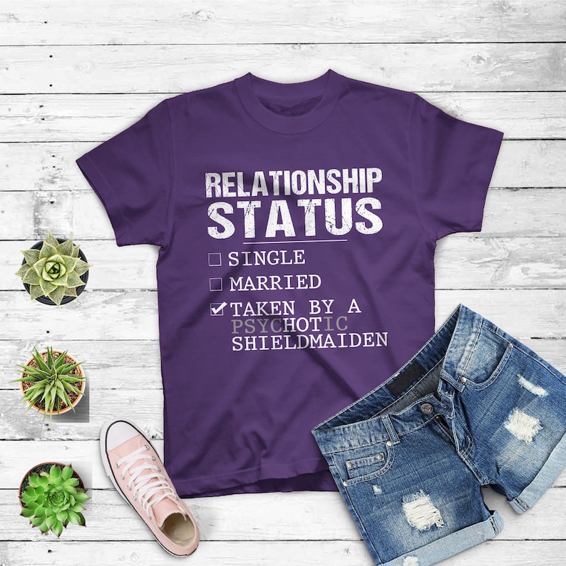 May include: Purple t-shirt with a white graphic that reads "Relationship Status" with a checkmark next to "Taken by a Psychotic Shieldmaiden" and unchecked boxes next to "Single" and "Married".