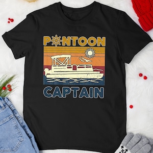 May include: Black t-shirt with a retro design featuring a pontoon boat, sun, and the words "PONTOON CAPTAIN" in a vintage font. The design includes a boat wheel and a sun graphic, evoking a nautical theme.