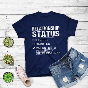 May include: Navy blue t-shirt with a white graphic that says "Relationship Status" with checkboxes for "Single", "Married", and "Taken by a Psychotic Shieldmaiden". The "Taken by a Psychotic Shieldmaiden" box is checked.