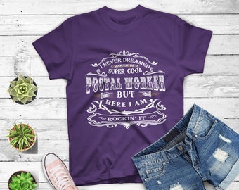 May include: Purple t-shirt with a white vintage-style graphic that reads "I never dreamed I would be a super cool postal worker but here I am rockin' it".