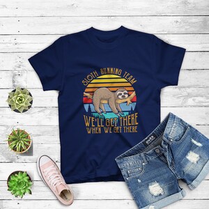 May include: A navy blue t-shirt with a vintage-style graphic of a sloth hanging on a branch. The graphic includes the text "Sloth Running Team" and "We'll Get There When We Get There".