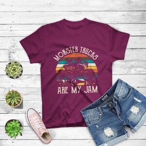 Puede incluir: Camiseta color burdeos con un gr&aacute;fico de estilo vintage de un cami&oacute;n monstruo conduciendo a trav&eacute;s de una puesta de sol. El texto "Monster Trucks Are My Jam" est&aacute; impreso en la camiseta.