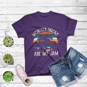 Puede incluir: Camiseta morada con un gr&aacute;fico de estilo vintage de un cami&oacute;n monstruo conduciendo a trav&eacute;s de una puesta de sol. El texto "Monster Trucks Are My Jam" est&aacute; impreso en la camiseta.