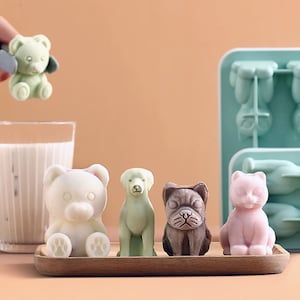 Op de afbeelding: Een set van vijf siliconen ijsblokjesvormen in de vorm van dieren. De vormen zijn lichtblauw en bevatten een beer, een hond, een kat, een bulldog en een beer. De ijsblokjes zijn bevroren in de vormen en klaar om te worden verwijderd.