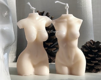 May include: Two white torso-shaped candles with a simple design. The candles are made of a smooth, white wax and have a slightly textured surface. The candles are sitting on a white surface.