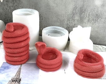 May include: Three silicone molds for making candles in the shape of a coiled snake. The molds are white and the snake is red.