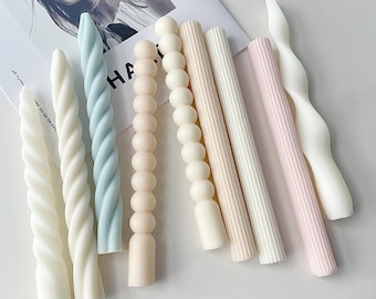 May include: Assortment of decorative candles in various colors and styles, including twisted, beaded, and ribbed designs. The candles are all white, light blue, and light pink.