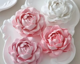 May include: Four decorative flower-shaped ornaments, three are pink and one is white, on a white plate with a decorative edge.