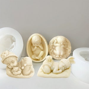 May include: Four silicone moulds for making baby-themed cake decorations. The moulds are white and feature different sleeping baby designs.