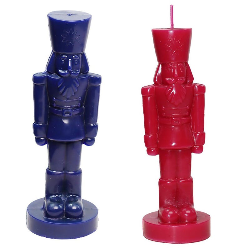 May include: Two nutcracker-shaped candles. One is a deep blue, the other is a vibrant red. Both candles have a detailed soldier design, including a hat, uniform, and base. A pink wick extends from the top of the red candle.