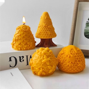 May include: Four yellow beeswax candles shaped like honeycombs and beehives. The candles are on a white surface with the word "MAG" printed on it.