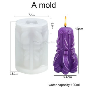 May include: A white silicone candle mold with a detailed design. The mold is 7.4 cm wide, 11.1 cm tall, and 6.9 cm deep. The mold is shown next to a purple candle with a detailed design. The candle is 10 cm tall and 6.4 cm wide. The candle mold has a water capacity of 120 ml.