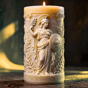 May include: A cream-colored pillar candle with a sculpted relief of a classical figure holding a shield and a sprig of leaves. The candle has a Greek key design at the base and a lit flame at the top. The candle is a decorative item.