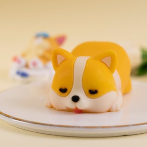 Puede incluir: Un molde para pastel de corgi durmiendo amarillo y blanco. El molde está hecho de silicona y tiene un diseño realista.