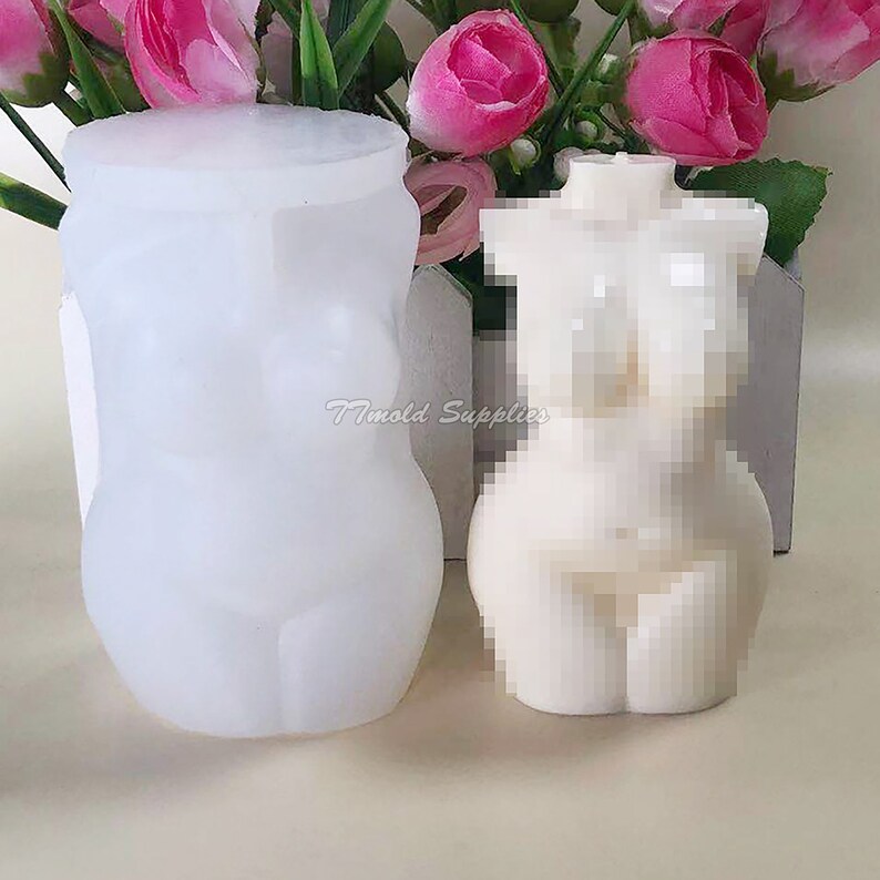 Op de afbeelding: Twee witte siliconen mallen voor het maken van kaarsen of zeep. De mal aan de linkerkant is gevormd als een vrouwelijk torso. De mal aan de rechterkant is een afgewerkte kaars in de vorm van een vrouwelijk torso.