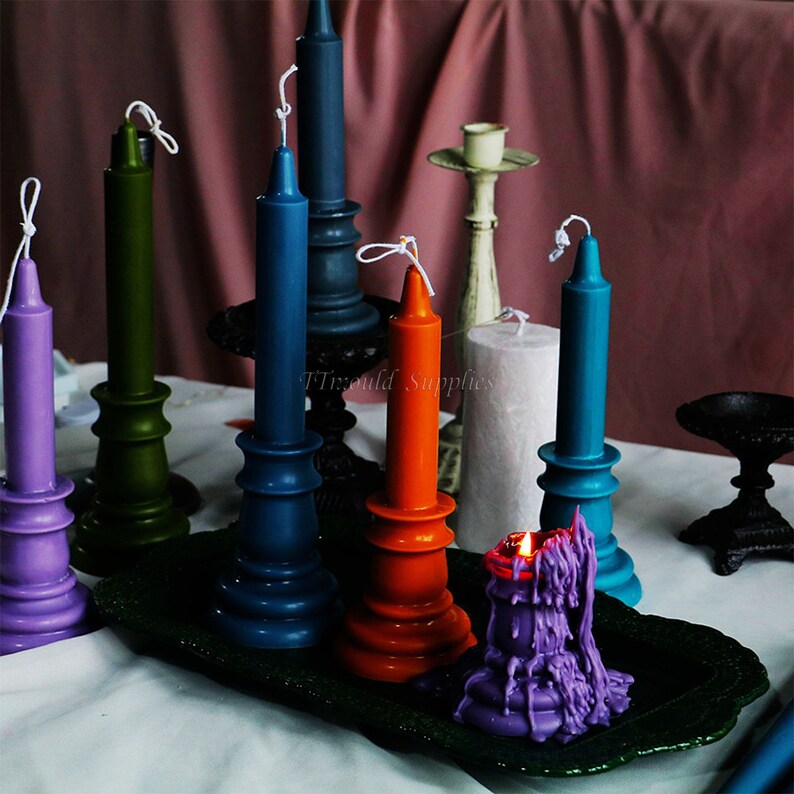 May include: A collection of colorful candles on decorative candle holders. The candles are in shades of purple, green, blue, orange, and teal. The candle holders are made of metal and have a vintage look. The candles are arranged on a dark green tray.